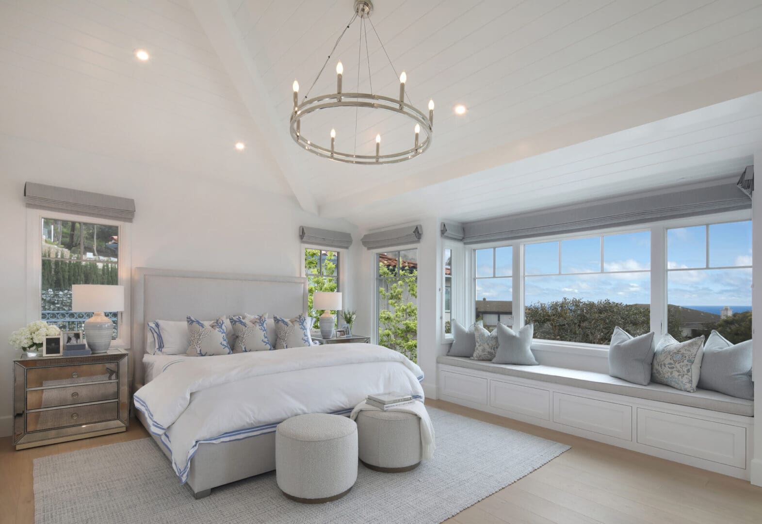 A white bedroom with a large window overlooking the ocean.